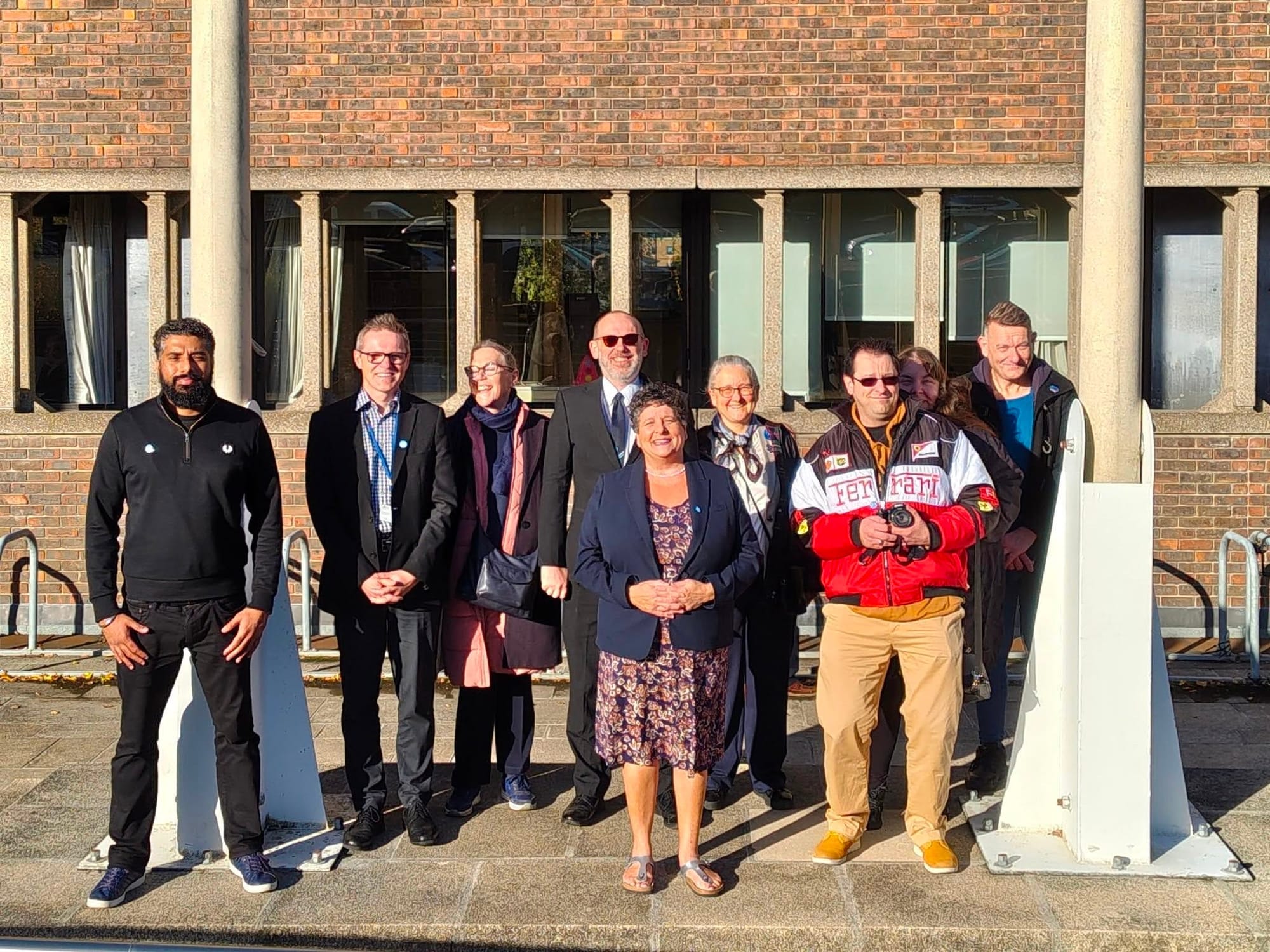 A group of people are stood in front of two flag poles. They are all smiling at the camera.